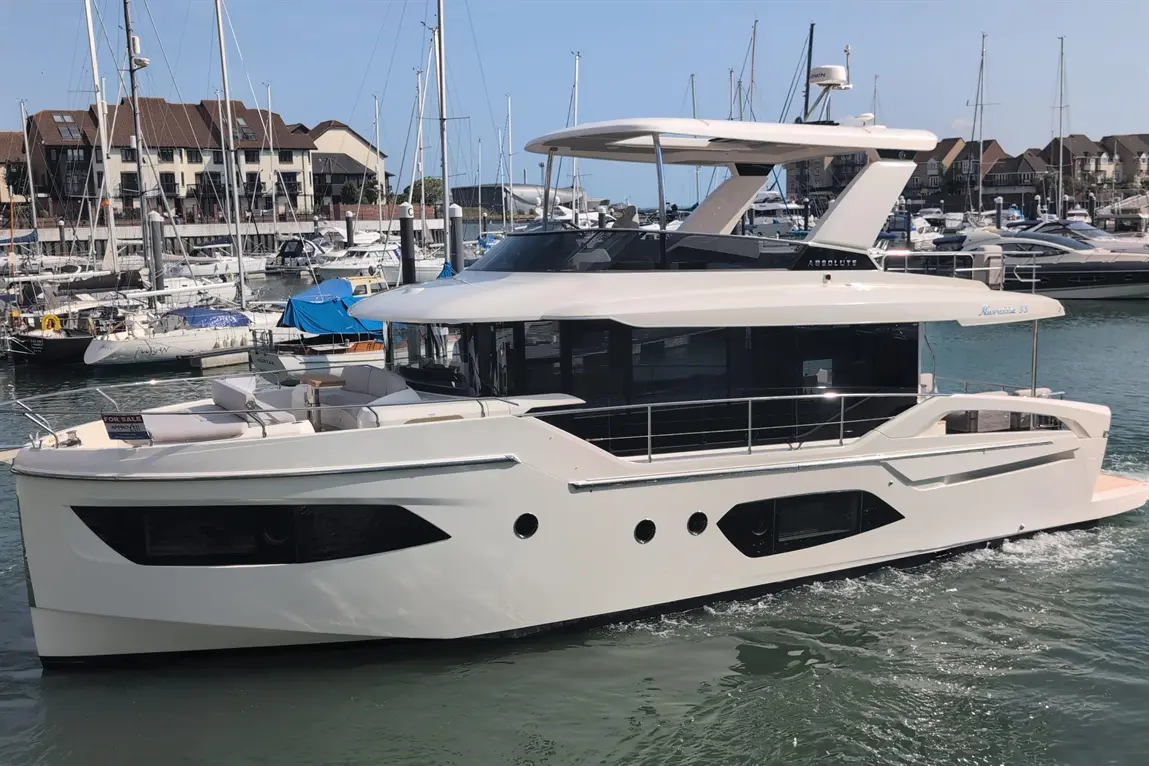 White luxury motorboat "Navetta 33" with spacious deck, moored at a marina surrounded by other boats and buildings.